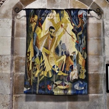 Tapestry hanging against a stone wall, depicting a saint catching an arrow in front of and deer